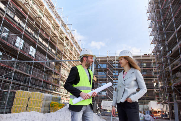istock An architect or civil engineer with planning documents meets with a customer or colleague on the large construction site and both of them wear white protective helmets. 1324696906