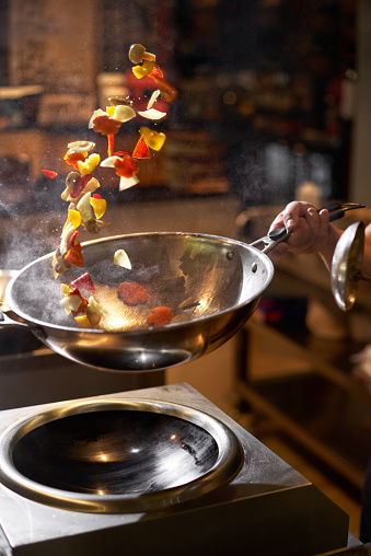 Chef hand keep wok. Closeup hands tossing food at professional dark kitchen. Chef in prepare asian food. Food delivery concept, fast food
