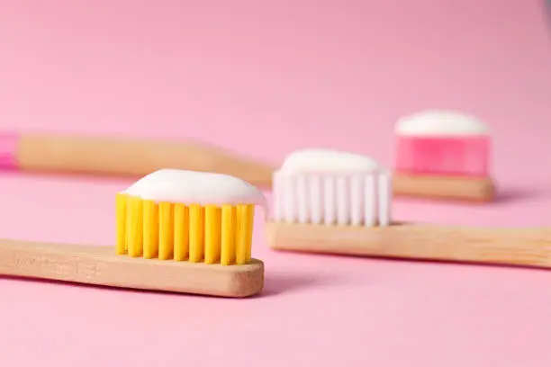 Wooden brushes with toothpaste on pink background, closeup