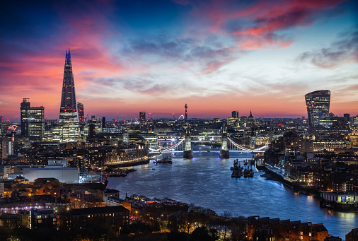 Elevated, panoramic view to the lit skyline of London, United Kingdom, just after sunset with Tower Bridge and modern office buildings along the Thames river