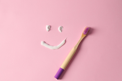 Funny face made with toothpaste and brush on pink background, flat lay