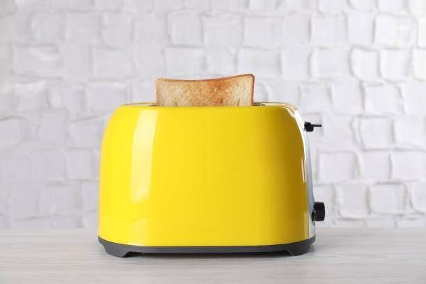 Modern toaster with slice of bread on white wooden table Modern toaster with slice of bread on white wooden table toaster stock pictures, royalty-free photos & images