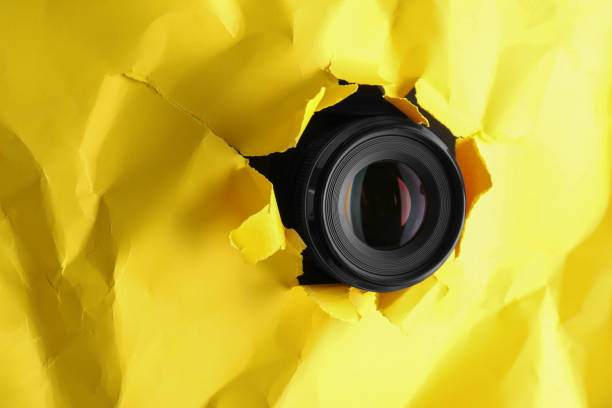 istock Hidden camera spying through torn hole in yellow paper, space for text 1324701591