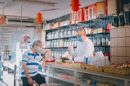 Asian chinese male pharmacist cutting ginseng chinese herbs medicine for his senior patient at traditional chinese herbal medicine shop