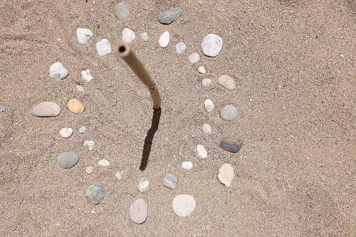 Sundial is lined with stones on sand of sea beach closeup background.