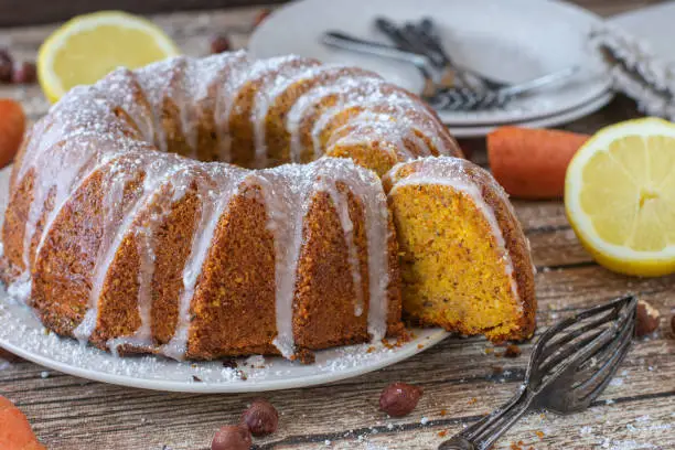 Juicy hazelnut carrot bundt cake with lemon glaze served on a rustic and wooden table background. Closeup and front view