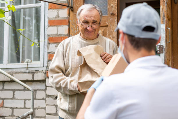 istock An elderly woman using a walker receives meals from a man working with a benevolent group delivering food to those who are at high risk because of the coronavirus COVID19. 1324706624