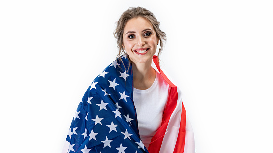 Portrait of fashion adult girl in white shirt at the studio with gray light background. Concept with copy space. She is holding American flag in the hands