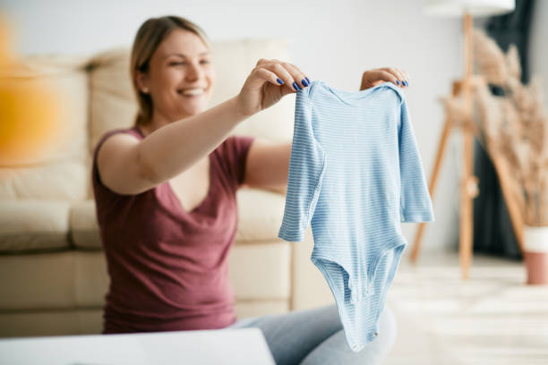 Close-up of woman holding baby's bodysuit at home. Close-up of mother holding baby bodysuit for boys at home. baby clothing stock pictures, royalty-free photos & images