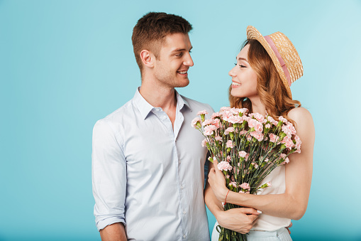 Image of young happy caucasian people man and woman isolated over blue background holding flowers.