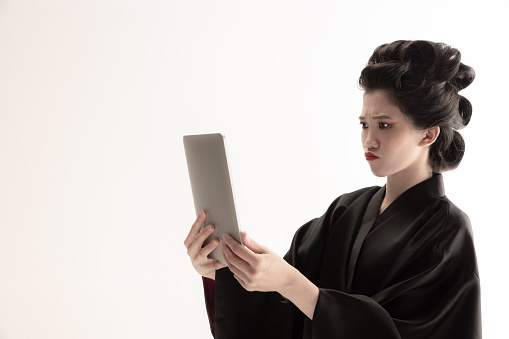 Portrait of young beautiful Japanese, woman in national attire kimono with tablet isolated over white background.. Concept of traditions, national flavour and culture, beauty. Copy space for ad.