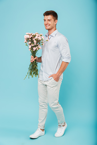 Image of young caucasian man isolated over blue background holding flowers.