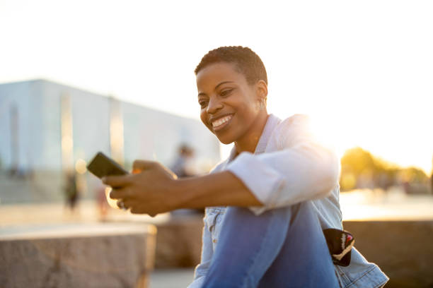 istock Smiling young woman using smartphone outdoors 1324717141