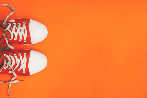 Youth sneakers on an orange background with copy space. Red sneakers with loose laces. Minimal style. Top view, flat lay.