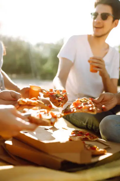 Photo of Hands taking slices of pizza close view. Group of Friends eating pizza at the beach.