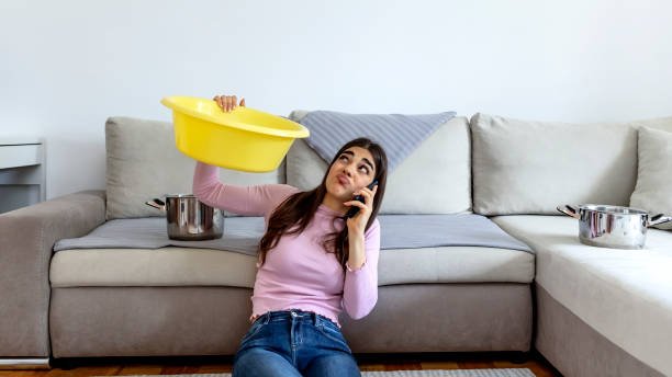 istock Woman looking up and holding pot under leaking ceiling. 1324723646