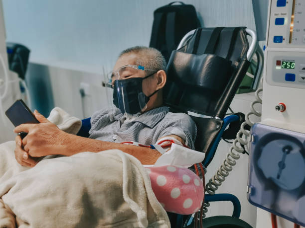 homme senior chinois asiatique en fauteuil roulant avec écran facial , masque facial sous traitement de dialyse à l’hôpital à l’aide d’un téléphone intelligent - dialyse photos et images de collection