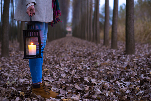 Woman with candle lantern walking in the woods at autumn night.