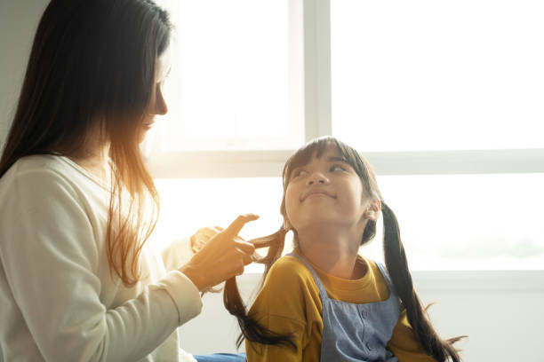 istock Asian mom making hair braid for daughter while sitting on bed at home. 1324727174