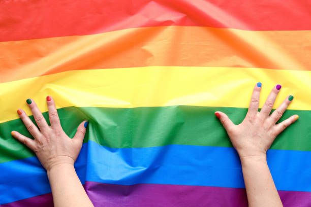 Happy Pride Month. Simple, minimal LGBT pride flag decor. Human hands with rainbow painted nails on top of stripy flag in colors of the rainbow. Flat lay, top view, minimal casual design. feliz mes del orgullo. decoración simple y mínima de la bandera del orgullo lgbt. manos con uñas pintadas de arco iris en la parte superior de la bandera de rayas en los colores del arco iris. lay plana, vista superior, diseño casual mínimo