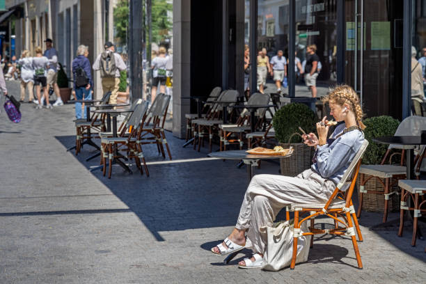 Young woman enjoying the sun, checking her phone and having a snack in the pedestrian zone in the center of Copenhagen