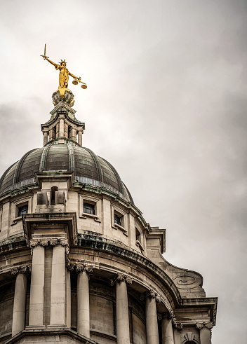 Storm clouds gathering above and around the statue of Lady Justice on the top of the main dome of the Royal Courts of Justice, known as Old Bailey after the street name in the City of London.