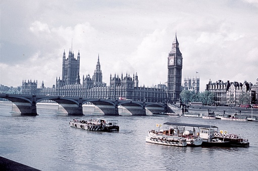 Palace of Westminster where Houses of Parliament meet along the Thames River, London, England.  Boats moored along the Albert Embankment in foreground. Photo taken August 7, 1967.