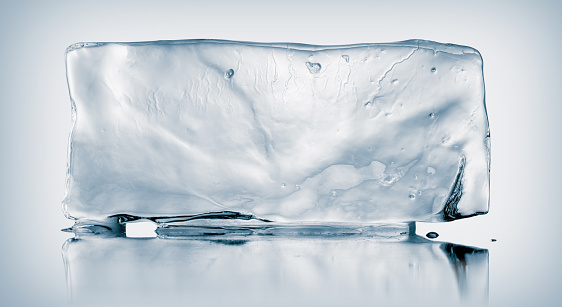 A large rectangle of melting clear ice, on white background with a mirror reflection. Creative concept of cold purity.