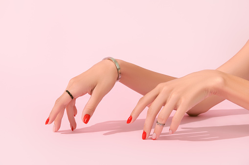 Womans hands with red manicure on pink background. Manicure design trends. Spring summer fashion accessories sale concept.