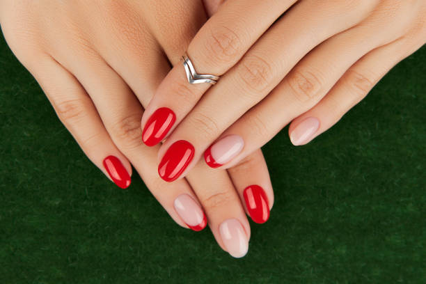 istock Womans hands with red modern manicure over green background. Manicure design trends. 1324739528
