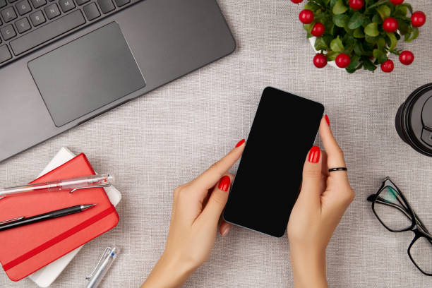 istock Woman with red manicure holding mobile phone on gray table 1324739668