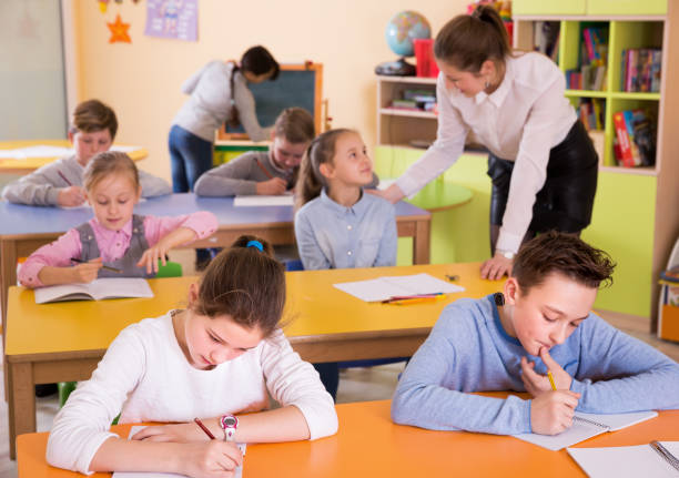 bambini 9-10 anni che lavorano a tavola, insegnante donna aiuta - 12 13 years immagine foto e immagini stock