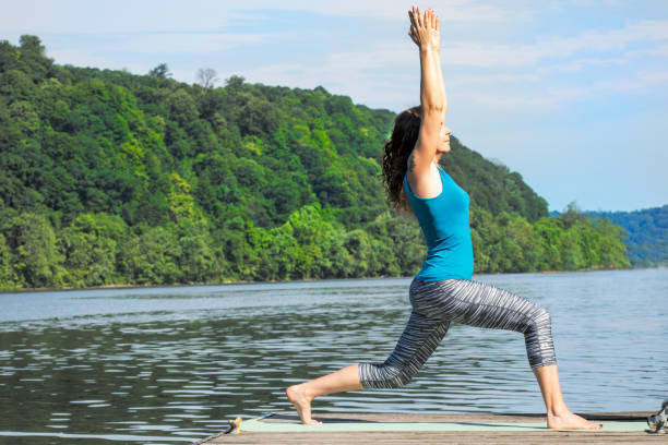 A beautiful 40 year old Caucasian woman in the Warrior I yoga pose outdoors in the morning by the Ohio River.