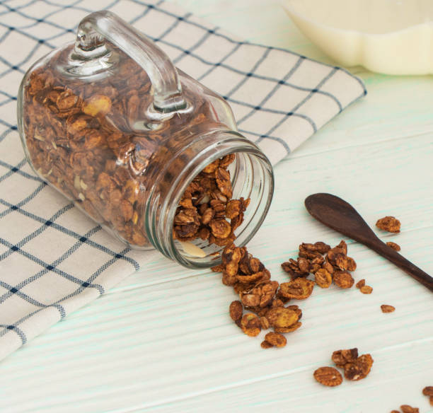 istock chocolate granola scattered from a glass jar mug on a wooden table. 1324742726