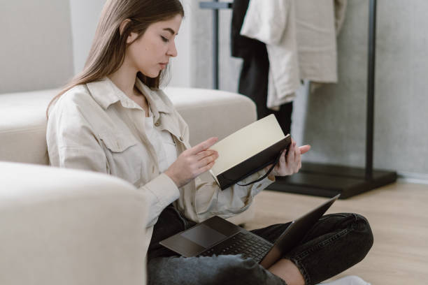 istock Young woman sitting on floor, holding notepad in hands 1324748093