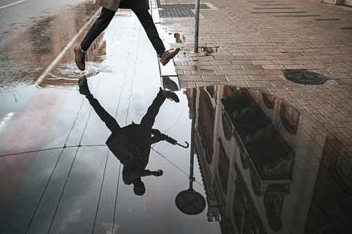 Low section of a man walking down the wet street with reflection in the water