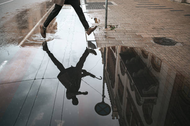Low section of a man walking down the wet street with reflection in the water Low section of a man walking down the wet street with reflection in the water puddle stock pictures, royalty-free photos & images
