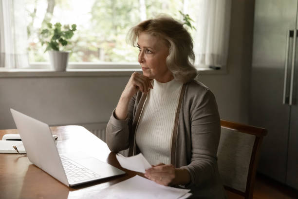 istock Pensive old woman work on laptop with documents 1324756601