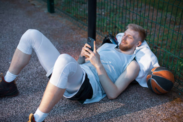 istock Basketball player sportive young guy lying with phone using social networks apps having break outdoors on sports court 1324757505