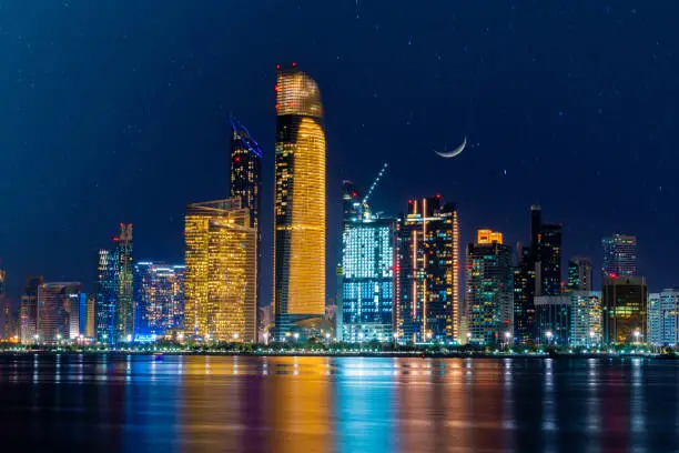 Night view of Abu Dhabi financial district skyline with moon in the sky. Luxury lifestyle hotels and business of United Arab Emirates.