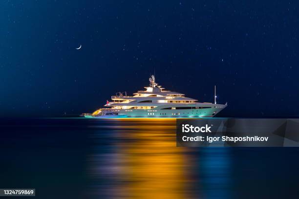 Night View To Large Illuminated White Boat Located Over Horizon Colorful Lights Coming From Yacht Reflect On The Surface Of The The Gulf Sea Shot At Blue Hour Stock Photo - Download Image Now