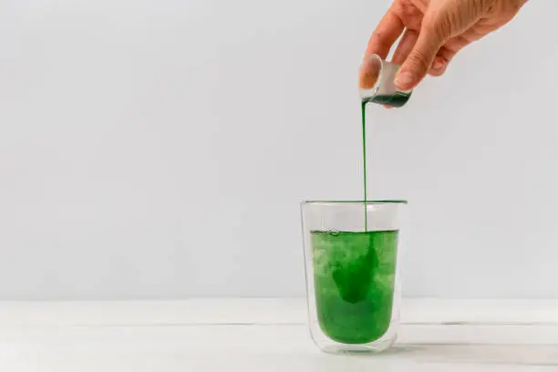 Woman hand pouring liquid chlorophyll in a glass cup. White background with space for text