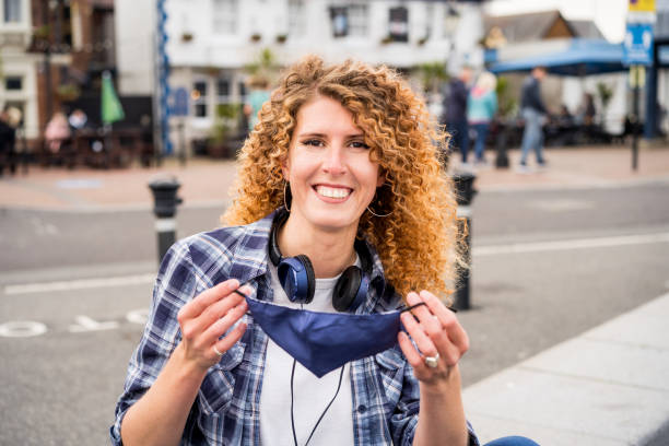 Young happy caucasian woman takes off a protective face-covering mask outdoors against European city background. Pandemic Covid-19 is over concept. Selective focus. Young happy caucasian woman takes off a protective face-covering mask outdoors against European city background. Pandemic Covid-19 is over concept. Selective focus happy end stock pictures, royalty-free photos & images