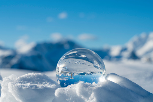 Frozen winter landscape on sunny day at Velika Planina, mirroring in Christal lens ball, clear blue sky,  high pasture plateau,  Slovenia.