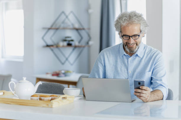 istock Mature man is using a laptop at the table in the living room 1324766449