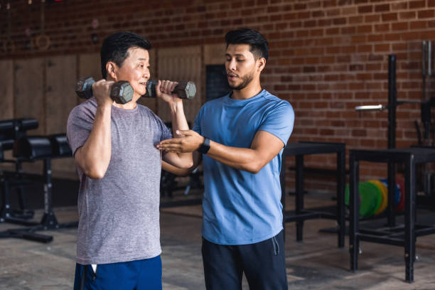 Personal trainer helps senior man with weights A mid adult male personal trainer helps an active senior man use hand weights while working out in a cross training gym. personal trainer stock pictures, royalty-free photos & images