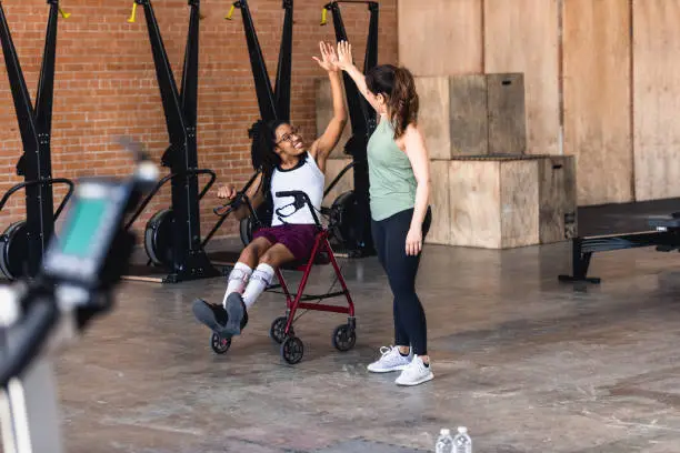 A young female athlete with a disability high fives a female personal trainer or physical therapist after a good workout.