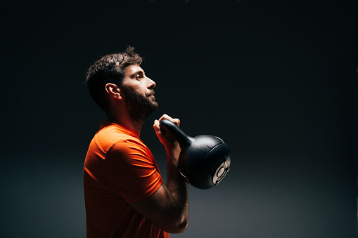 Sporty man using kettlebells during a stength training over a black wall