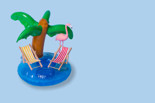 istock Creative summer idea with inflatable palm ring, deck chairs and exotic flamingo bird on pastel blue background. 1324772546