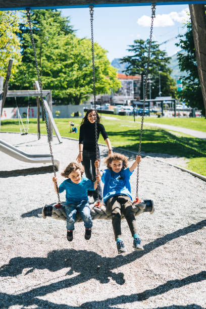 mãe empurra meninos em balanços no playground - child swing swinging balance - fotografias e filmes do acervo